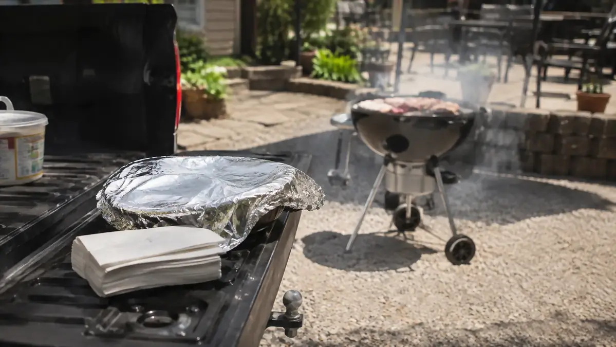 A pickup tailgate with a foil-covered platter balanced on the edge, no table in sight