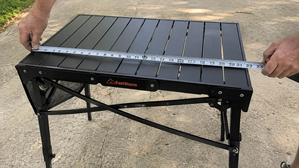 Hands holding a tape measure across the top of a small folding grill table showing it is smaller than expected